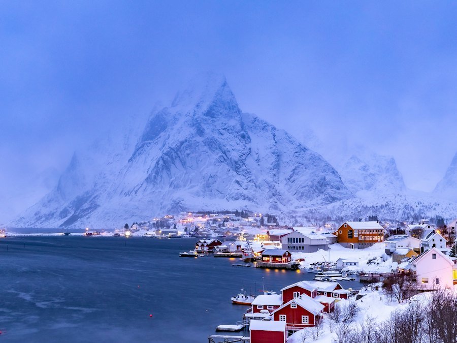 Snowy fjord village with red wooden houses beneath mountains at dusk