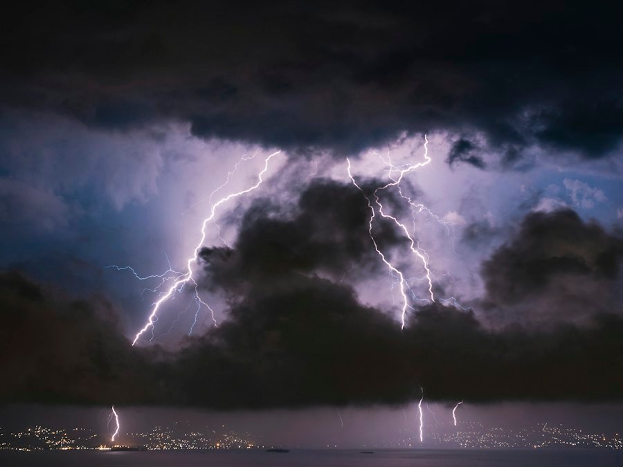 Lightning bolts striking from storm clouds above a city skyline at night