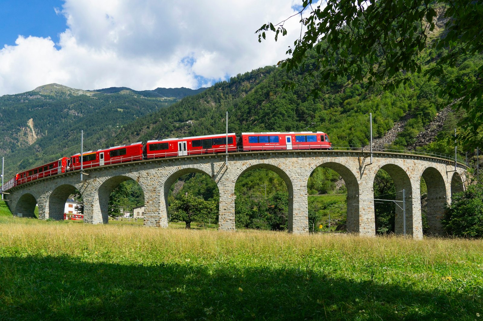 The red Bernina train crossing a stone viaduct in the Swiss mountains